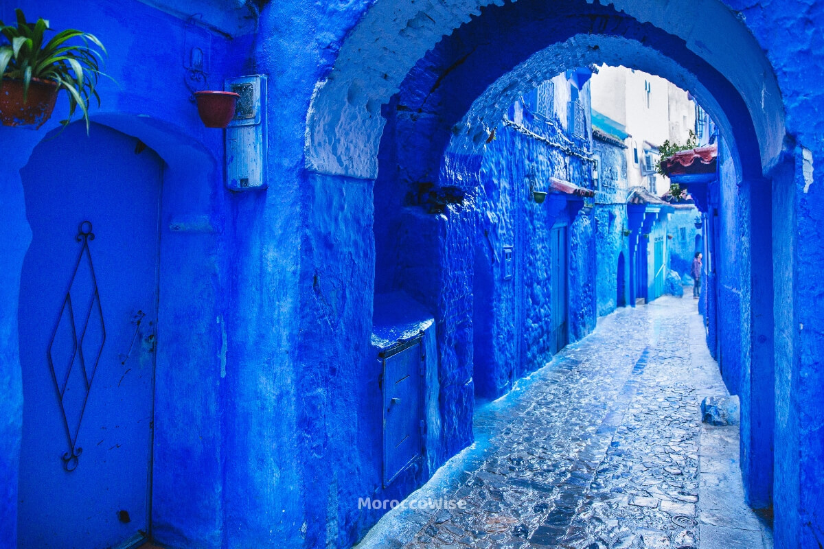 A stepped blue alley in Chefchaouen with the Rif Mountains nearby